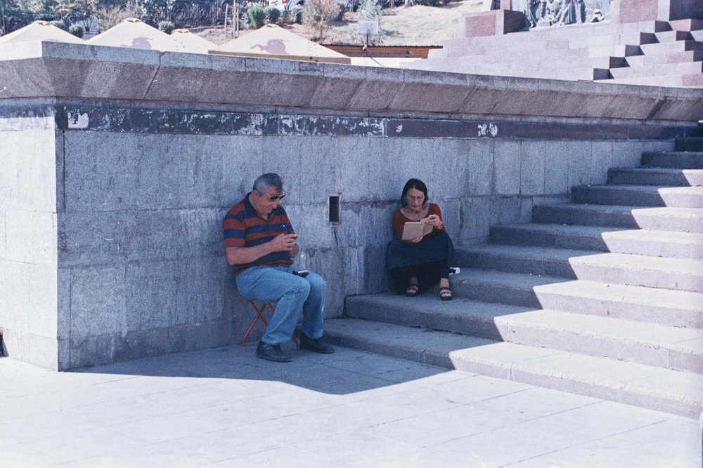 man and a woman sitting in the shadow reading a book